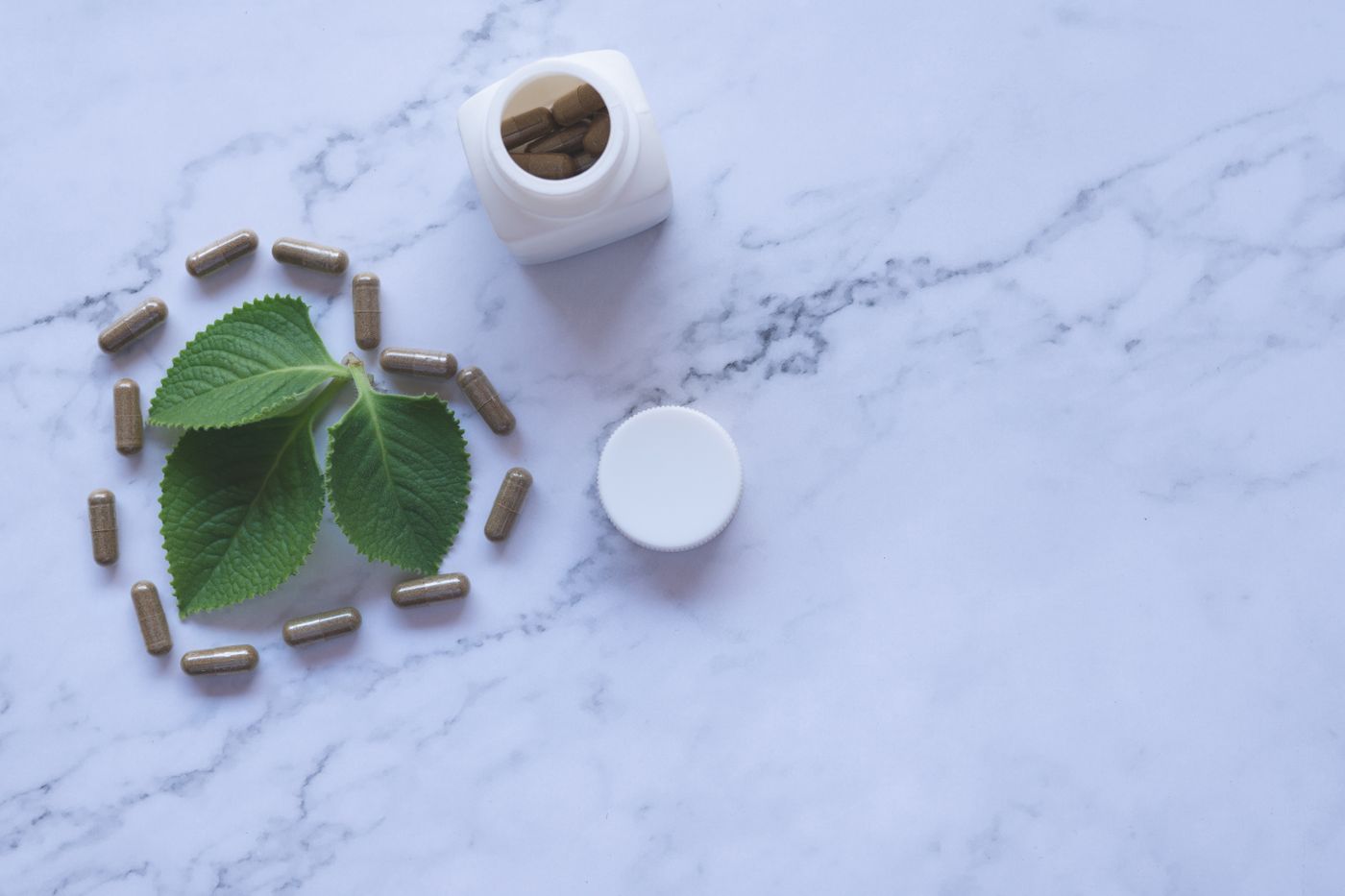 Bote de cápsulas de ashwagandha con una hoja verde sobre una superficie de mármol