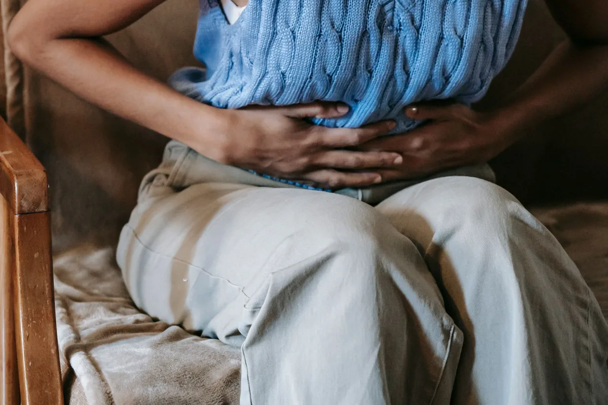 Mujer sentada en un sofá con las manos sobre el abdomen por dolor de estómago