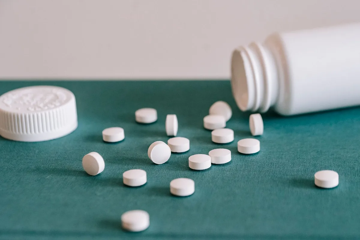 Comprimidos blancos saliendo de un bote de medicamento sobre una superficie de color